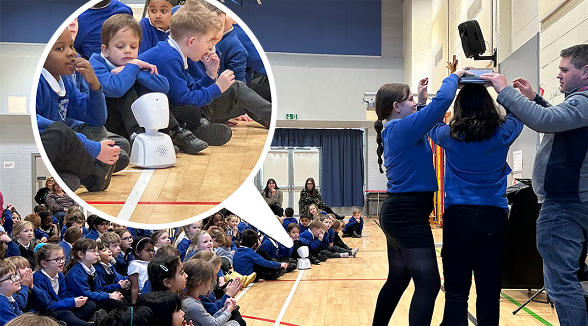 Children watching a school assembly, a small robot sits in the front row