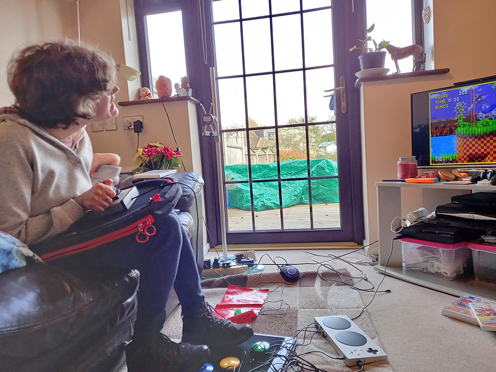 Seated young woman plays retro video game using foot and hand gaming controls