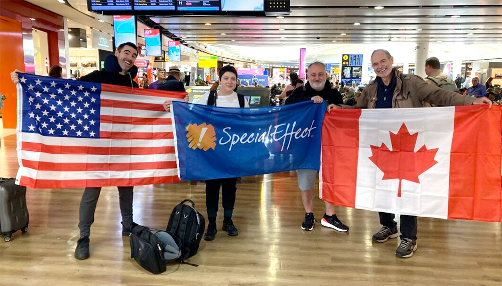 Four people in an airport holding SpecialEffect, US and Canadian flags