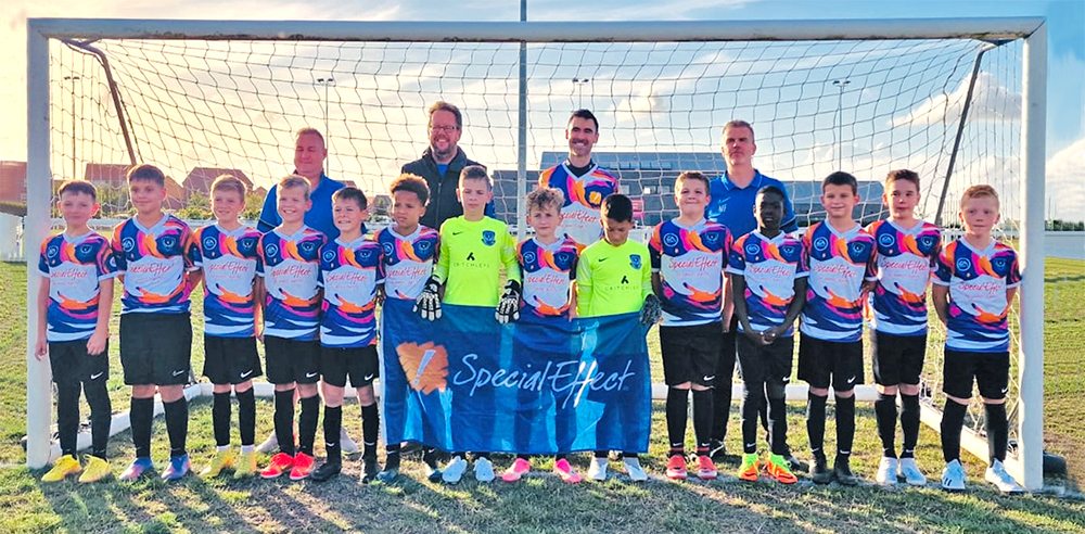 Boy's soccer team lined up in front of a goal with three adults standing behind them